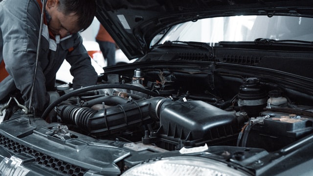 Mechanic inspecting and working under the hood of a car during engine maintenance in an auto repair shop.