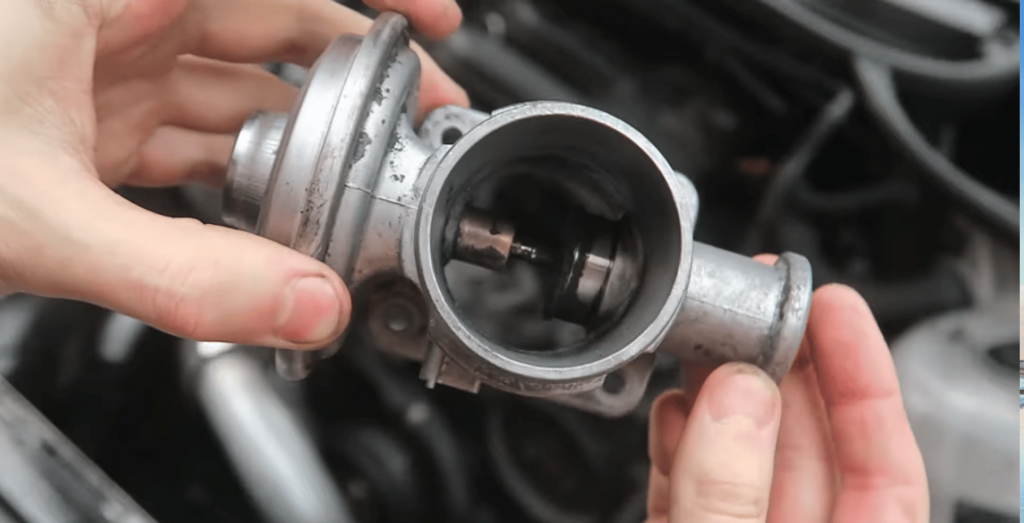 Hands holding a used EGR (Exhaust Gas Recirculation) valve removed from a vehicle engine.