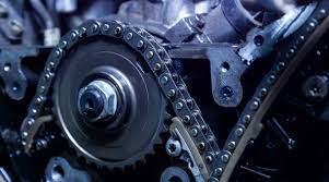 Close-up view of a mechanical timing chain system in an engine, showing gears and metal components in blue lighting.