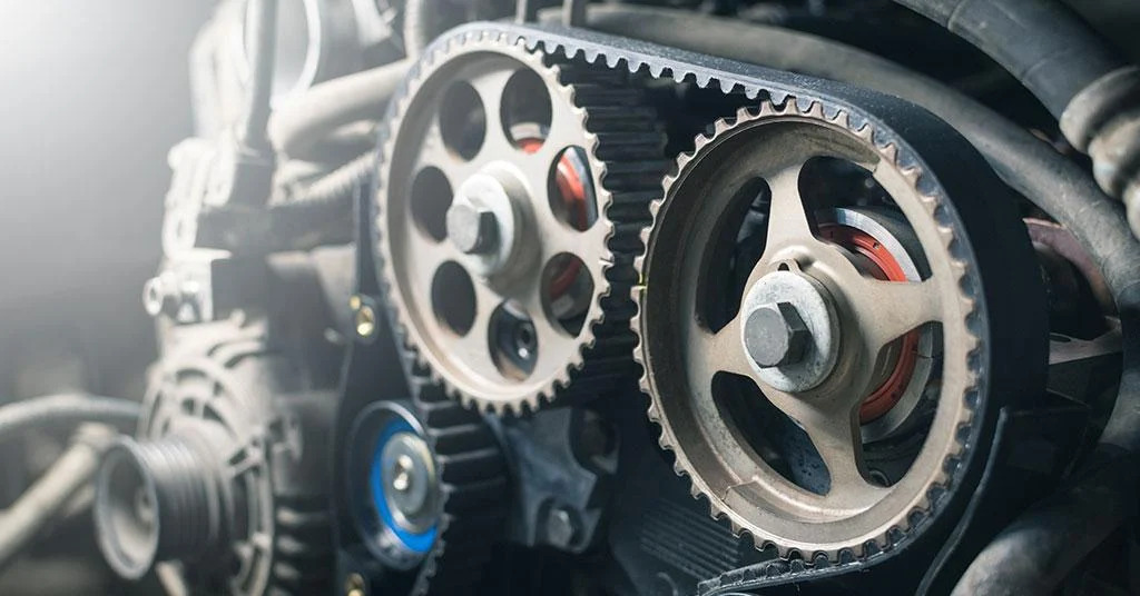 Close-up view of an engine timing belt and camshaft gears inside a car engine compartment.